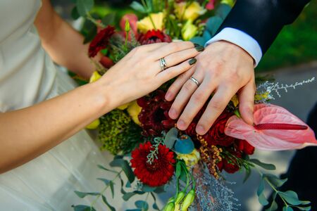 Newlywed couple holding hands and displaying wedding rings, close up. Hands and rings on the background of wedding bouquet.の写真素材