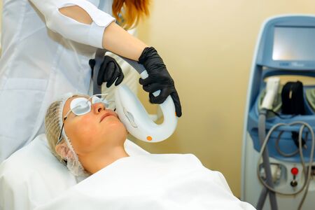 Beautiful woman in cosmetic clinic during photo rejuvenation procedure. Anti acne phototherapy with professional equipment. Laser face skin treatment in a beauty salon. Hardware cosmetology.の写真素材