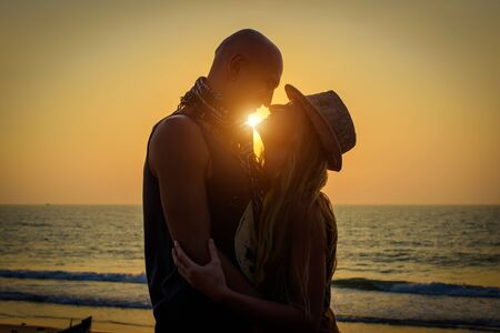 Stylish loving couple hugging each other on the beach at sunset. Man and woman in holiday honeymoon trip.の写真素材
