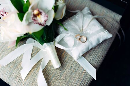 Gold wedding rings on a white cushion decorated with ribbons and flowers, close-up. Wedding theme, accessories for newlyweds.の写真素材