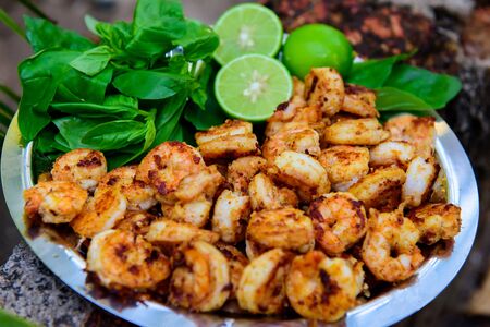 Shrimp fried with garlic salt and pepper on a large platter with lime and herbs, close up. Plate of delicious grilled prawns is decorated with fresh Basil branches. Seafood restaurant outdoor.の写真素材