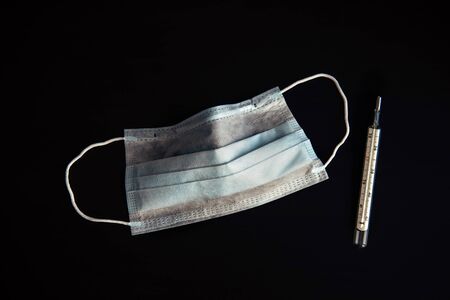 Medical mask and thermometer isolated on black background, close-up. Quarantine, incubation period...