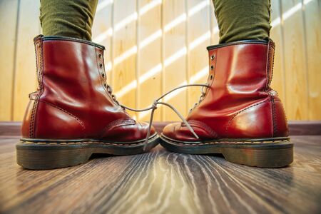 Human legs in stylish bright red boots with thick white laces tied together on wooden background, close-up. April Fools' day, pranks and fun.の写真素材