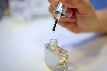 Female hand holding transparent nail Polish, blurred background, close-up. Bottle of clear nail polish with brush.の写真素材