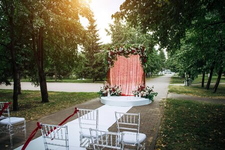 Arch decorated with fresh flowers and fabric for wedding ceremony outdoor. Solemn wedding registration in the park.の写真素材