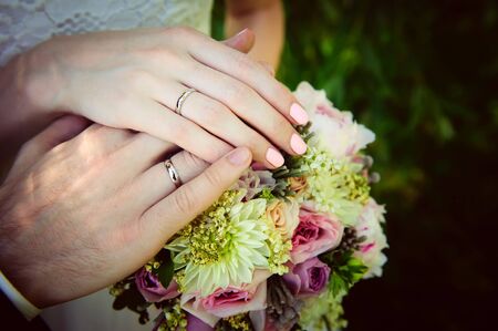 Hands of newlyweds on the background of wedding bouquet. Gold wedding rings on the finger of bride...