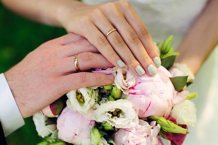 Hands of newlyweds on the background of wedding bouquet. Gold wedding rings on the finger of bride...