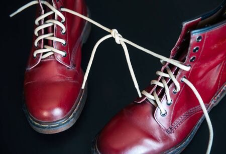 Stylish red shoes with laces linked together on black background. High boots with shoelaces connected together, close-up. Concept of April fool's day, joke, prank.の写真素材