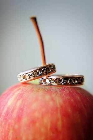 Two gold wedding rings on red apple, close-up. Vintage rings for bride and groom, selective focus. Concept of the wedding party and family.の写真素材