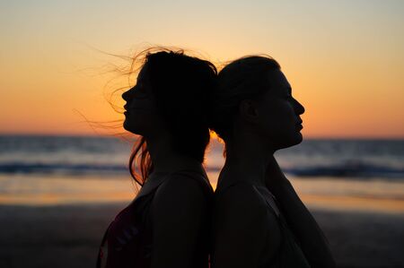 Close up silhouette of womens couple in romantic scene of sunset over the sea. Beautiful female young lesbian couple in love.の写真素材
