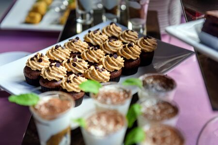 Chocolate cupcakes with cream on banquet table, close-up. Catering events. Sweet table, buffet, bakery, confectionery. Handmade cakes.の写真素材