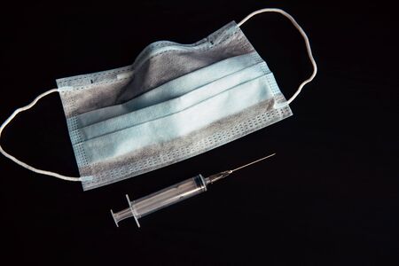 Medical face mask, disposable syringe isolated on black background, close-up. Medical supplies with space for text. Epidemic season, vaccination, flu, quarantine, prevention.の写真素材