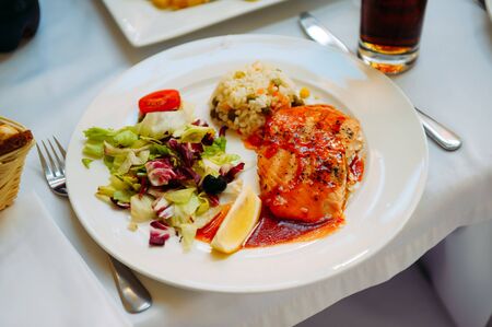 Grilled salmon with sauce, rice and vegetables on a white plate. Gala dinner in the restaurant. Banquet service.の写真素材