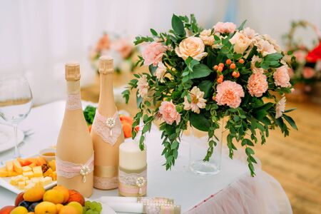 Beautiful festive table for the newlyweds, close-up. Champagne bottles are decorated with lace. Flowers, candles, glasses, snacks, fruit. Concept of wedding celebration, banquet.の写真素材