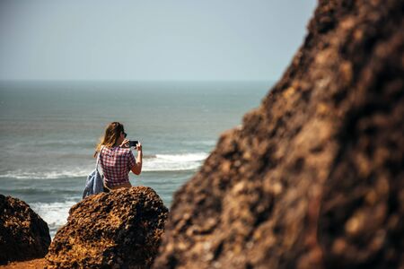 young woman hands use smartphone making photo and video sitting on a rock enjoying the beach and the...