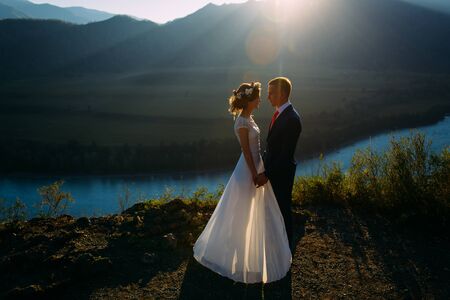 Happy wedding couple staying and kissing over the beautiful landscape with mountainsの写真素材