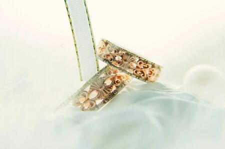 Vintage wedding rings among white ribbons, close-up. Gold rings with patterns on a blurred white...
