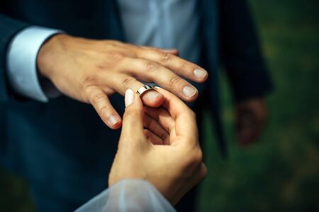 Young bride put a gold wedding ring on the groom's finger, close-up. Wedding ceremony, exchange of rings.の写真素材
