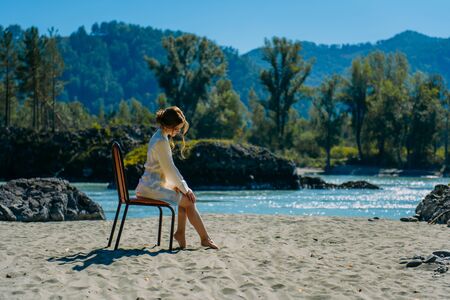 young woman in white short dress sitting on chair near river in wild natureの写真素材