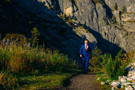 Young man in a business suit with red tie on the background of mountains goes to his aim on a sunny...