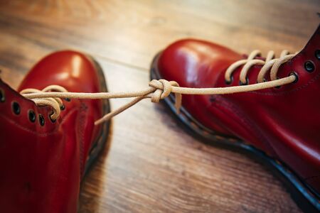 April Fools Day Shoes with laces tied together. Red boots on wooden background, copy space.の写真素材