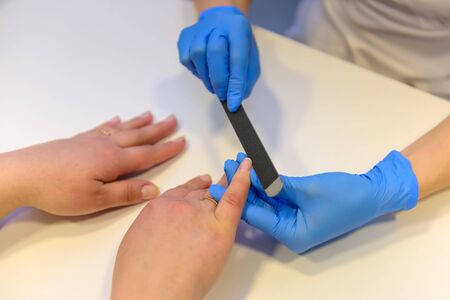 Nail care at beauty salon. Unknown woman gets a medical manicure in spa-center. Master of manicure in medic gloves nail file works. Healthy Fingernails.の写真素材