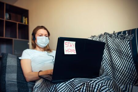 Woman in medical mask working on laptop online from home. Stay at home during a virus pandemic. Quarantine, self-isolation, disease prevention concept. Sticker with text.の写真素材