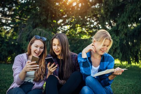 Cute girl students spend free time sitting on green grass in the park on summer day. One woman is...