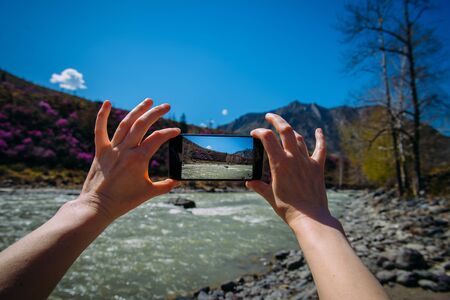 Close-up of hands holding smartphone and taking photo or video. Unknown person takes smartphone stunning mountain landscape on a sunny day. Focus on the gadget screen. Digital technologies in travel.の写真素材