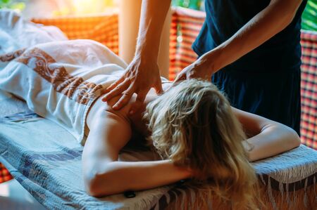 Back and shoulder massage close-up. Pain relief with massage. Young girl lies on special table during session of wellness massage outdoor.の写真素材