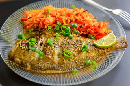 Baked fish flounder with lemon, carrot and spicy herbs, in a plate closeup on a black background. Delicious fish dish with vegetables for healthy and proper nutrition.の写真素材