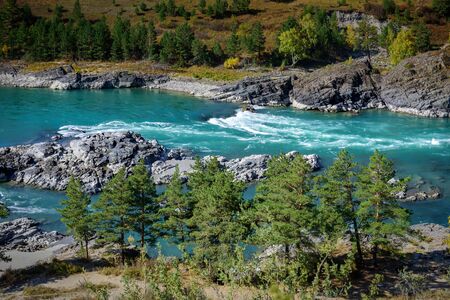 Powerful stream of water, rocky shores overgrown with grass and trees. Turquoise mountain river on sunny autumn day. Magnificent natural landscape.の写真素材