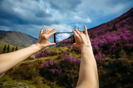 Close-up of smartphone in hands. Unknown woman using a gadget takes photos of a mountain slope...