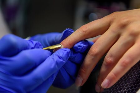 Cuticle removal, close-up. Manicure in the salon. Manicurist in blue gloves shifts the cuticle of the nail with metal spatula.の写真素材