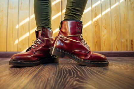 Human legs in stylish bright red boots with thick white laces tied together on wooden background, close-up. April Fools' day, pranks and fun.の写真素材
