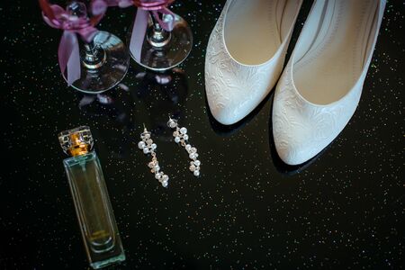 Beautiful set of wedding accessories bride. Morning bride's. White shoes, pearl earrings, and perfume on a shiny black surface.の写真素材