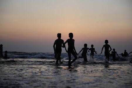 Silhouettes of children jumping in the surf on the background of the sea and evening sky. Boyish figures, children playing on seashore. Carefree childhood, concepts of freedom and the future.の写真素材