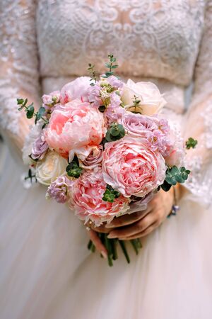Stylish bride in a white dress holds an unusual wedding bouquet close-up. Delicate wedding bouquet of different flowers in the hands of the bride, selective focus.の写真素材