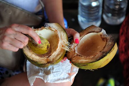 Eating a green coconut, indian traditional way without spoon or tools. Close-up of woman hands in process of scraping the coconut flesh from peel.の写真素材