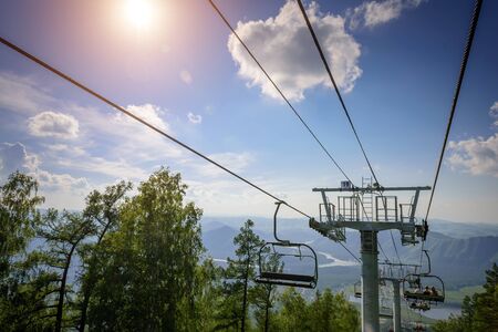 Ski lift in the mountains on sunny day against blue sky, white clouds, green hills and mountain lake. Mountain valley with cable car, view from top. Ski resort in summer.の写真素材