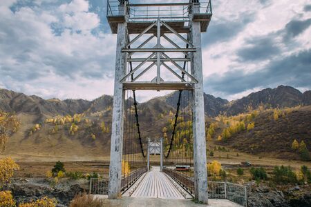 Metal bridge over river on mountains and storm clouds background. Combined pedestrian and road bridge over the river in the highlands. Auto travel around the world.の写真素材