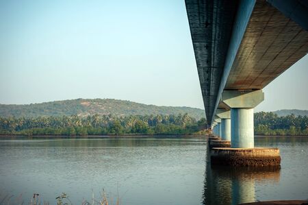 Long road bridge over the river, side view. Powerful stone columns of bridge are reflected in the...