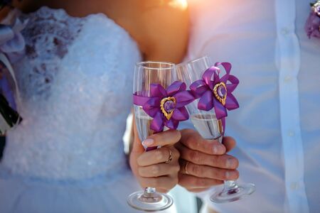 Bride and groom holding glasses of champagne in their hands, close-up. Glasses decorated with ribbons. Newlyweds clinking glasses at wedding reception.の写真素材