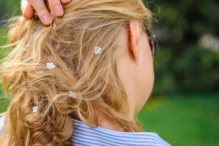 Back view of a woman hair with small white flowers on green blurred background. Blonde touches her...