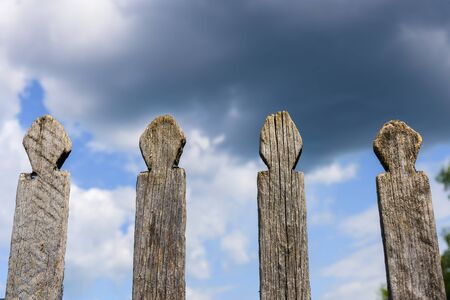 Old wooden fence against sky with clouds. Dilapidated village fence on a cloudy day. Silence and...