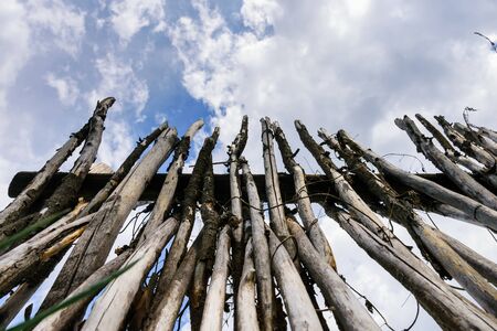 Sharp stakes of palisade stand upright against cloudy sky, view from below. Old village fence made...