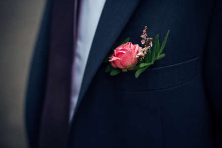 Boutonniere of fresh flowers on the suit of groom. Red rose in a buttonhole, close-up.の写真素材