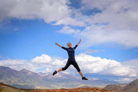 Young woman enjoying life and jumping against blue sky and mountains background. Happy female...