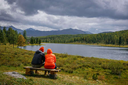 Couple in hooded jackets sitting on a bench, backs to the camera against the backdrop of beautiful...