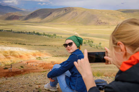 Female tourist takes photos of her girlfriend on smartphone at a beautiful vantage point, close up,...